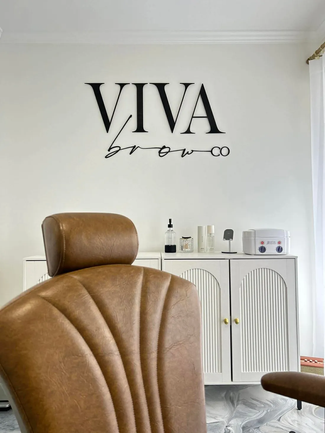 A Viva Brow sign mounted above a leather treatment chair in a beauty studio.